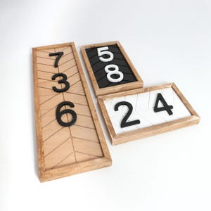 May include: Wooden address number signs with black numbers. One sign has the numbers 736 on a light wood background with a geometric pattern. The other signs have the numbers 58 and 24 on black and white backgrounds.