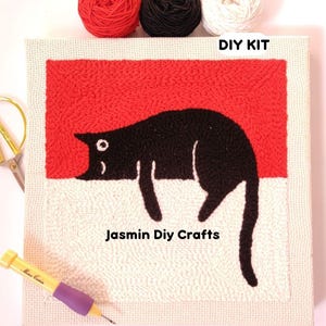 May include: DIY craft kit featuring a black cat design on a red and white background. The kit includes three yarn balls in red, black, and white, along with a punch needle and scissors. The text "DIY KIT" and "Jasmin DIY Crafts" are visible.