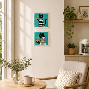 May include: Two square punch needle wall art pieces featuring black cats wearing white and black striped shirts, each holding a yellow mug with steam, set against a vibrant teal background. The textured fiber art is displayed vertically.