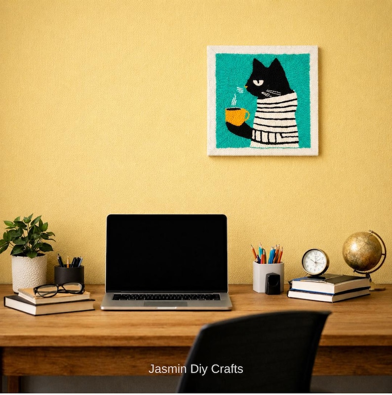 May include: A square wall art piece featuring a black cat wearing a white and black striped sweater, holding a yellow mug with steam rising. The cat is set against a bright teal background with a white border, displayed on a yellow wall.