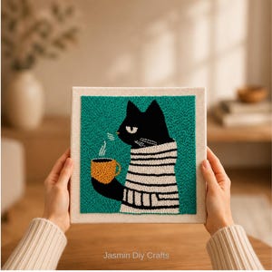 May include: A square punch needle embroidery art piece on a cream fabric frame featuring a black cat wearing a white and black striped sweater, holding a yellow mug with steam rising, set against a solid teal background with text Jasmin Diy Crafts.