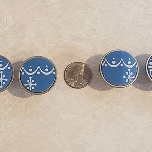 May include: Four blue and silver round cabinet knobs with a white snowflake design. The knobs have a raised edge and a smooth surface.
