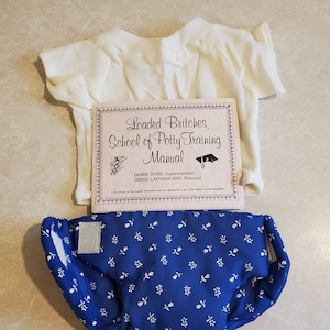 May include: A white t-shirt and blue diaper with white flowers printed on it. The diaper is labeled "Loaded Britches School of Potty Training Manual" with the names "Debbie Iford, Superintendent" and "Debbie Laffranchini, Principal".