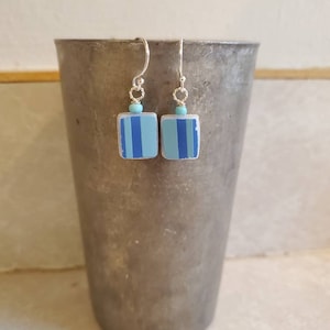Puede incluir: Un par de pendientes de plata con colgantes cuadrados rayados en azul y turquesa.