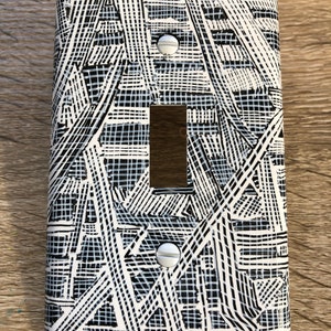 Pode incluir: Uma tampa de interruptor de luz branca com um padrão geométrico preto e branco.