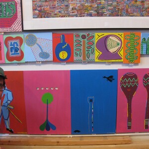 May include: A wall display of colorful, framed artwork featuring abstract designs, geometric shapes, and whimsical illustrations. The artwork is displayed in a grid pattern and includes a variety of colors, including red, blue, green, yellow, and purple.