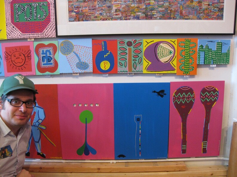 May include: A wall display of colorful, framed artwork featuring abstract designs, geometric shapes, and whimsical illustrations. The artwork is displayed in a grid pattern and includes a variety of colors, including red, blue, green, yellow, and purple.