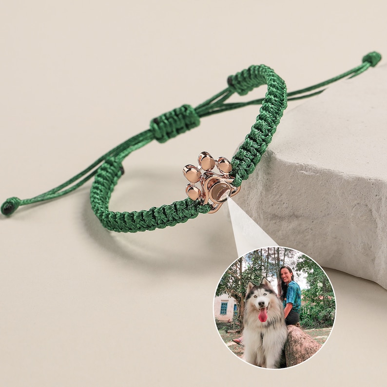 May include: A green braided bracelet with a rose gold paw print charm. The bracelet is adjustable and has a sliding knot closure.