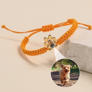 May include: Orange braided bracelet with a gold paw print charm. The charm has a small clear crystal in the center.