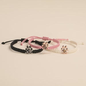May include: Three braided bracelets with paw print charms. The bracelets are black, pink, and white.