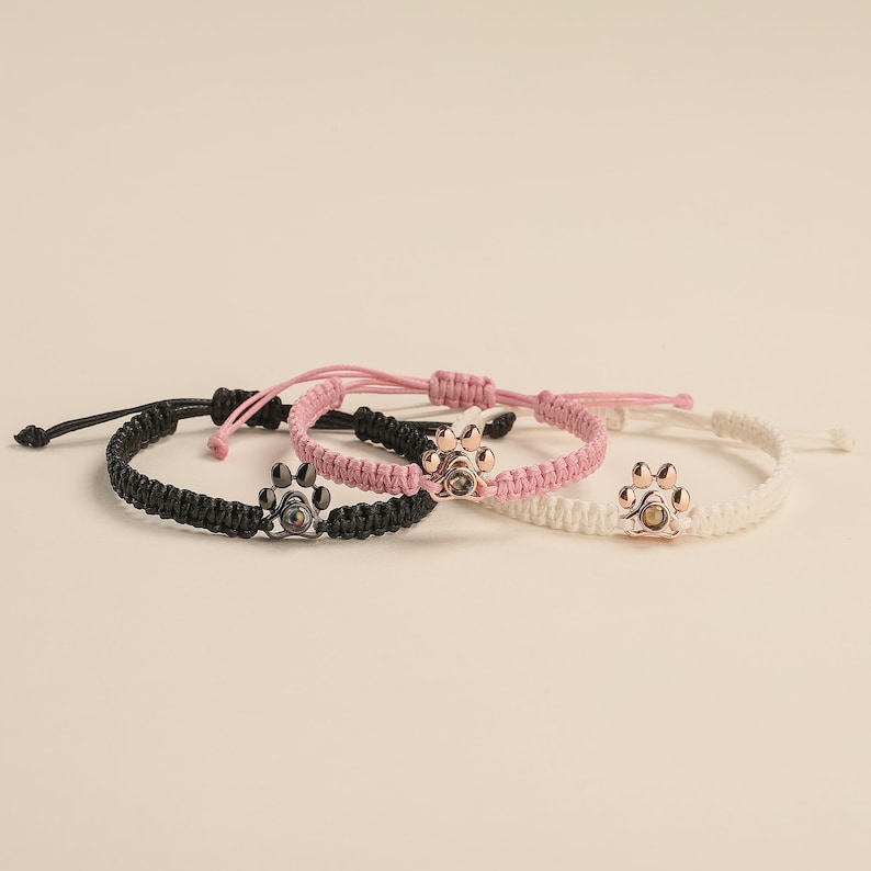 May include: Three braided bracelets with paw print charms. The bracelets are black, pink, and white.