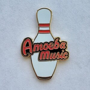 以下が含まれることがあります： 「Amoeba Music」の文字が赤と黒で書かれた、ボウリングのピンの形をしたピンバッジ。ピンは白地に赤と黒のストライプ、金の縁取りです。