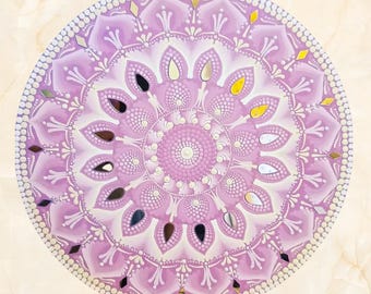 May include: A round, hand-painted mandala in shades of lavender and white, featuring intricate floral patterns and small mirrored accents. The design is symmetrical, with a central circular motif and a dotted border.