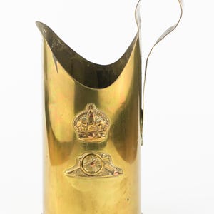 Puede incluir: Un letrero de madera rústico blanco con la palabra "Welcome" escrita a mano. El letrero tiene un aspecto envejecido y un elemento floral decorativo. El fondo es una textura de madera borrosa.