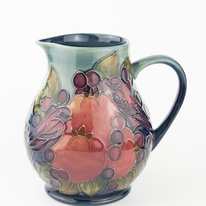 May include: A white ceramic mug with a black handle and the text "But First, Coffee" in a black, handwritten-style font. The mug is on a white surface.