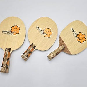 May include: Three ping pong paddles with light wood faces and patterned handles. Each paddle features a honeycomb graphic and the text "NANO700.3C7 The Best by Quality Made in Korea."