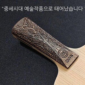 May include: A wooden table tennis paddle with a detailed, intricate design on the handle. The handle is labeled "ONVN" and has a small circle with the letters "WTB" inside. The paddle is made of light wood.