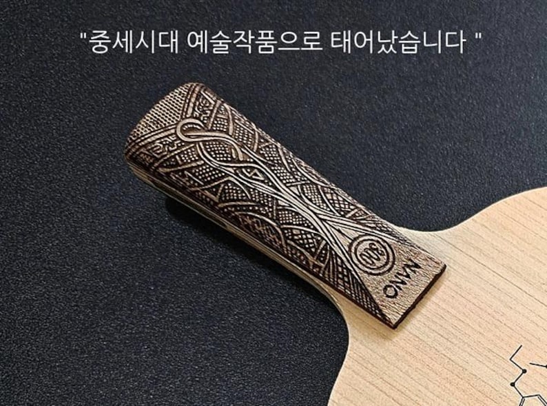 May include: A wooden table tennis paddle with a detailed, intricate design on the handle. The handle is labeled "ONVN" and has a small circle with the letters "WTB" inside. The paddle is made of light wood.