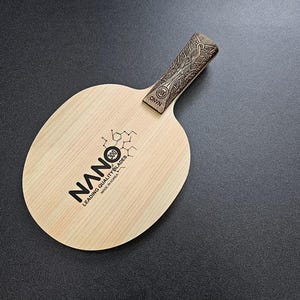 May include: A wooden table tennis paddle with a brown handle and a natural wood blade. The blade has the text "NANO 300 LEADING QUALITY BLADES MADE IN CHINA" printed on it.