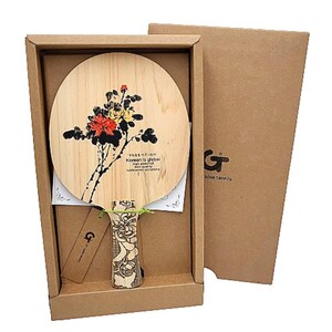May include: A wooden table tennis paddle with a floral design and the text "Korean is global" in a box. The paddle has a black and white floral design with red and yellow accents.