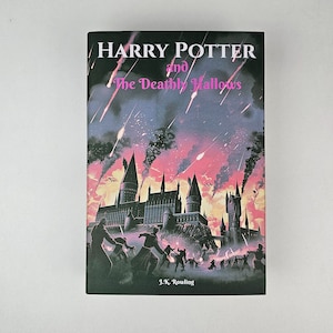 K&ouml;nnte beinhalten: Ein Buchcover f&uuml;r "Harry Potter und die Heiligt&uuml;mer des Todes" von J.K. Rowling. Das Cover zeigt eine dunkle Silhouette von Hogwarts mit einem rosa und violetten Himmel mit fallenden Sternen.