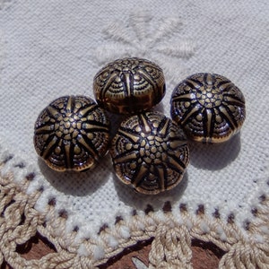 May include: Four gold-colored metal buttons with a starburst design. The buttons are on a white crocheted surface.