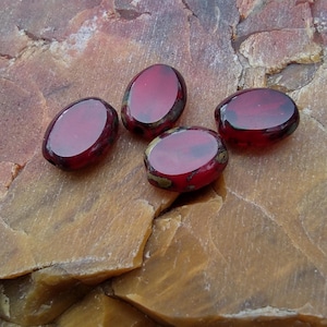 May include: Four red glass beads with gold flecks, displayed on a brown and yellow rock surface.