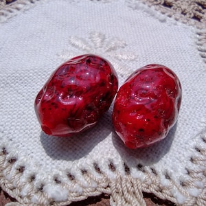 May include: Two red, shiny, heart-shaped stones on a white crocheted doily.