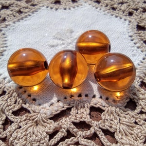 May include: Four amber glass beads on a white crocheted doily. The beads are round and have a smooth, shiny surface.