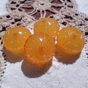 May include: Four amber-colored glass beads with a textured surface. The beads are round and have a slightly domed shape.