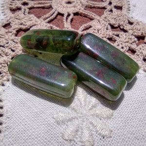 May include: Four green glass beads with red flecks, arranged on a white crocheted surface.