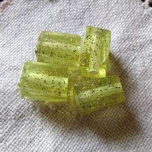 May include: A group of four green glass beads with gold glitter embedded in the glass. The beads are arranged in a pile on a white crocheted surface.