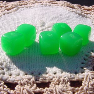 May include: Six green, translucent, cube-shaped beads. The beads are made of glass and have a smooth, polished finish.
