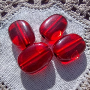 May include: Four red glass beads with a striped pattern. The beads are oval shaped and have a glossy finish.