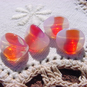 May include: Four glass beads with a pink and orange ombre effect. The beads are round and have a smooth, shiny surface.