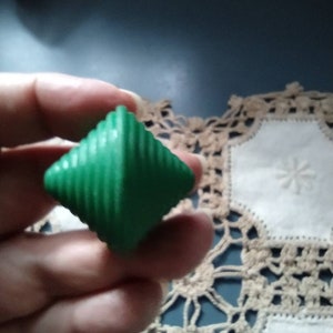 May include: A green, diamond-shaped, plastic toy with a spiral design. The toy is being held in a hand.