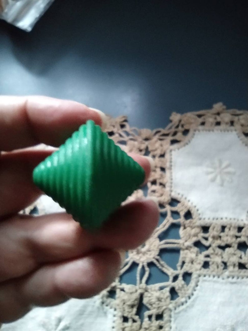 May include: A green, diamond-shaped, plastic toy with a spiral design. The toy is being held in a hand.
