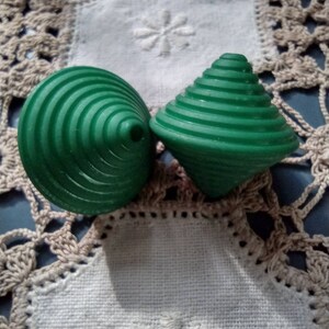 May include: Two green spinning tops with a ridged design. The tops are on a white crocheted doily.
