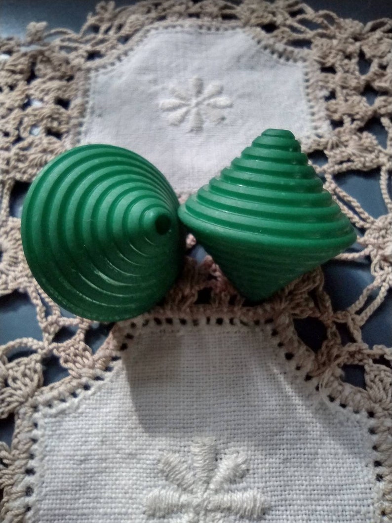 May include: Two green spinning tops with a ridged design. The tops are on a white crocheted doily.