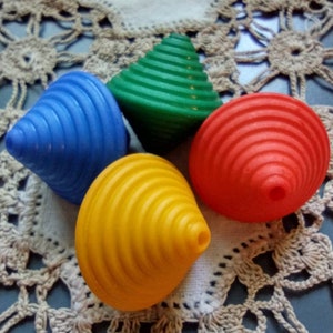May include: Four colorful spinning tops, one blue, one green, one yellow, and one red, are arranged on a white crocheted doily.
