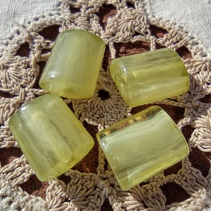 May include: Four translucent yellow glass beads with white swirls. The beads are cylindrical in shape and have a smooth, polished finish.