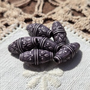 May include: A group of six purple and white ceramic beads with a decorative pattern. The beads are oval shaped and have a smooth, glossy finish.