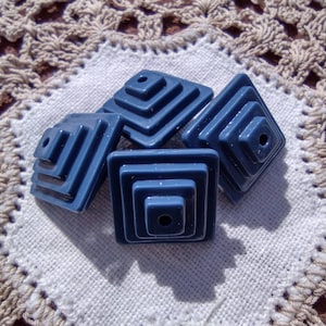 May include: Four blue plastic pyramid-shaped beads with a hole in the center of each. The beads are stacked on top of each other.