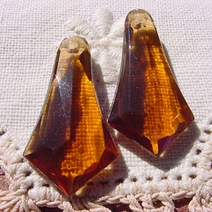 May include: Two amber glass teardrop-shaped pendants with a faceted design. The pendants have a hole at the top for stringing.