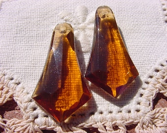 May include: Two amber glass teardrop-shaped pendants with a faceted design. The pendants have a hole at the top for stringing.