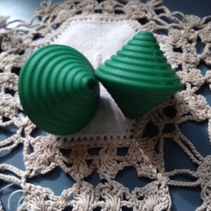 May include: Two green plastic spinning tops with a spiral design. The tops are on a white crocheted doily.