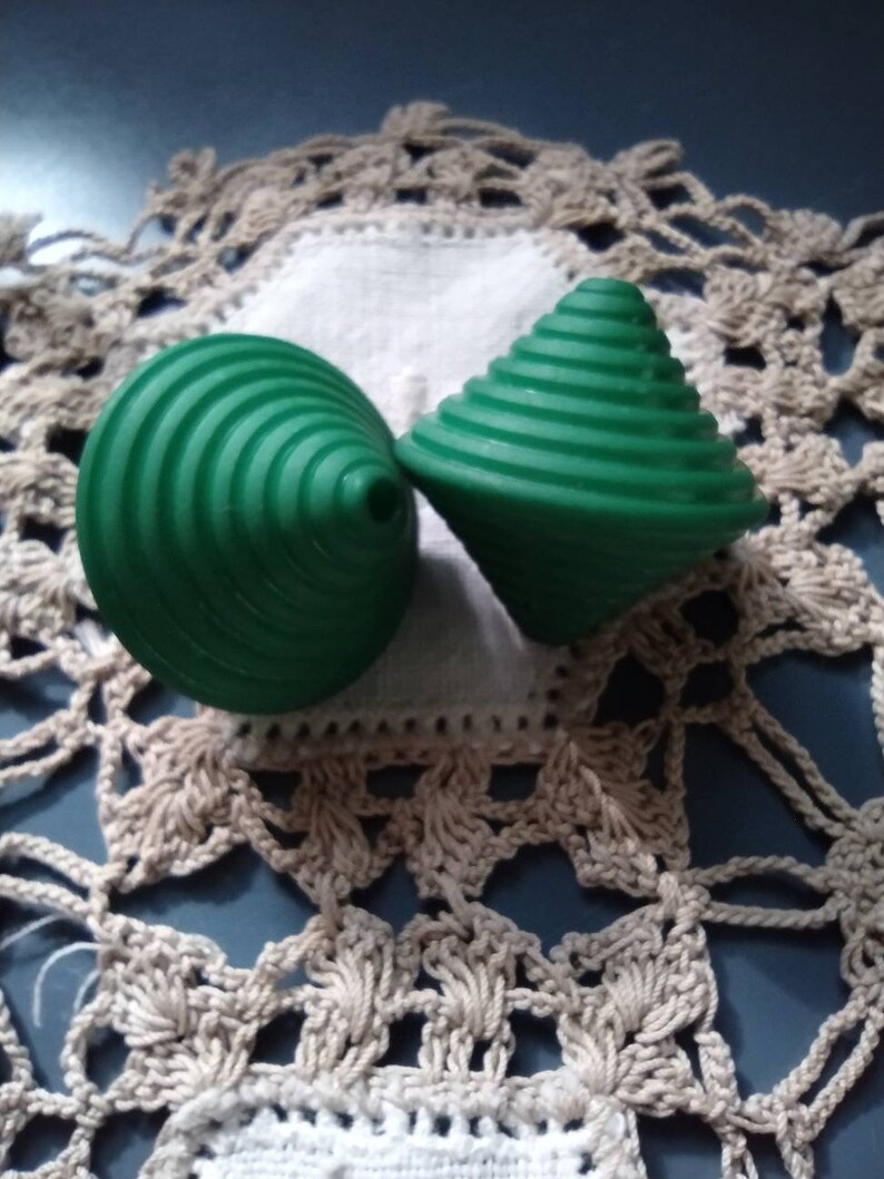May include: Two green plastic spinning tops with a spiral design. The tops are on a white crocheted doily.