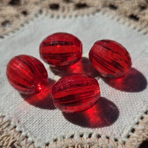 May include: Four red glass beads with a striped pattern. The beads are round and have a glossy finish.