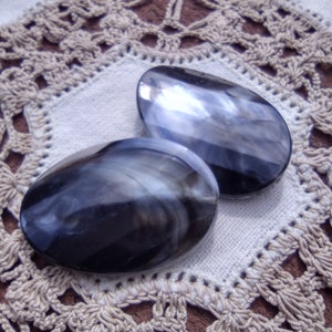 May include: Two black and white oval-shaped hair clips with a swirl pattern.