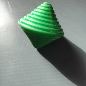 May include: A green plastic spinning top with a spiral design. The top is made of multiple layers of plastic that are stacked on top of each other.